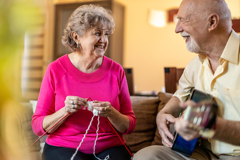 senior-couple-sitting-sofa-woman-knitting-man-playing-guitar