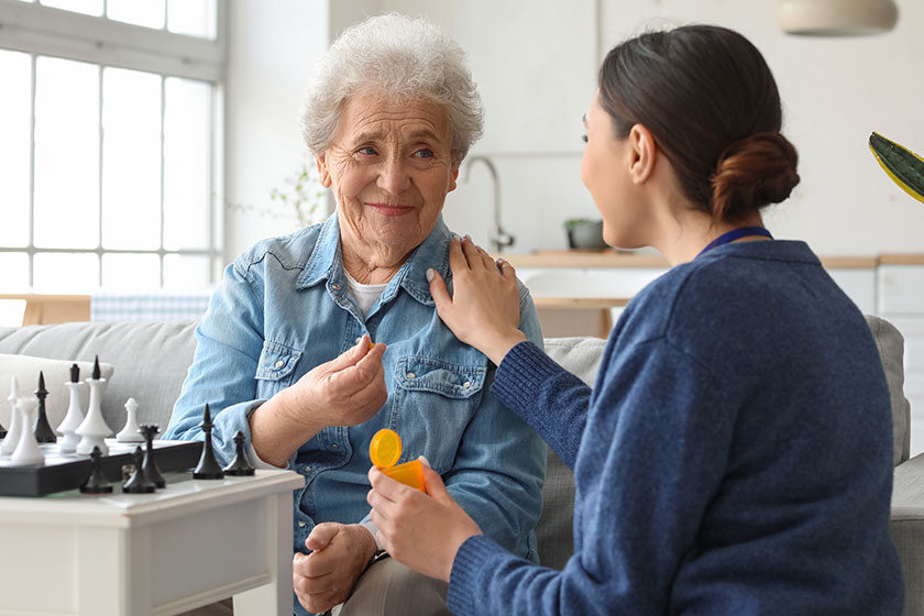 Senior woman taking pill from caregiver at home